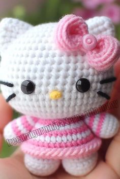 a small crocheted hello kitty doll in a pink and white dress is held by someone's hand