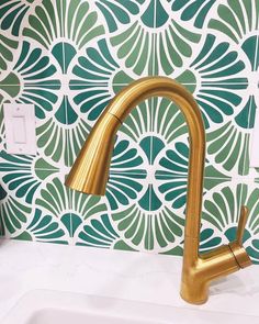 a gold faucet in front of a green and white wallpapered background