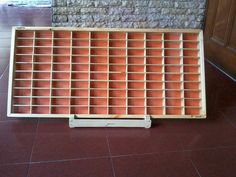 a wooden box with many compartments sitting on the floor in front of a brick wall