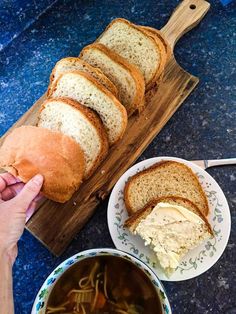 a person holding a piece of bread over a bowl of soup on a wooden cutting board