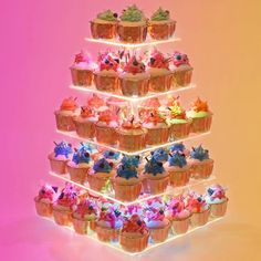 cupcakes are arranged in the shape of a tower with lights on them and frosting sprinkles