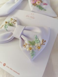 two white bow ties with flowers on them sitting on top of a piece of paper