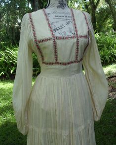 "This is a lovely, Romance Style Gunne Sax dress in a loosely woven, ecru-colored gauze with embroidered ribbon as an accent. It's beauty lies in its sumptuous skirting and simplicity. It is entirely lined in acetate excluding the 'poet sleeves' that are elasticized at the wrist. The bodice is in a square fashion that is accented by deep pink and magenta floral, embroidered ribbon that ends at the empire waist and the top of the shoulders The waist consists of the gauze fabric with two sashes to Embroidered Ribbon, Sax Dress, Square Fashion, Gunne Sax Dress, Gunne Sax, Gauze Fabric, Dress With Tie, Deep Pink, Empire Waist