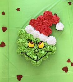 a green cake with red and white icing on it's face, surrounded by hearts