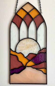 a stained glass window hanging on the wall with chains around it's edges and mountains in the background