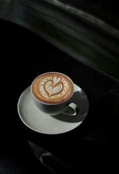 a cappuccino on a white saucer sitting on a black tablecloth