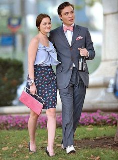 a man and woman dressed in formal wear walking together on the grass with pink purses