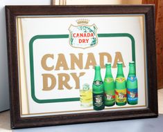 there is a sign that says canada dry and six bottles in front of it on the table