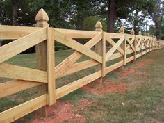 a wooden fence in the middle of a grassy area with trees and grass behind it