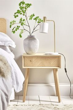 a bedroom with a bed, nightstand and plant on the night stand next to it