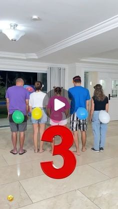 a group of people standing in a living room next to each other with balloons on the floor