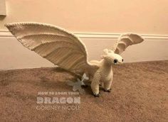 a white knitted dragon figurine sitting on the floor next to a wall