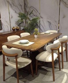 a wooden table with white chairs and plates on it in front of a marble wall