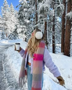 a woman standing in the snow holding a cup of coffee and scarf over her head