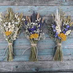 three bouquets of dried flowers tied together on a blue wooden background with twine