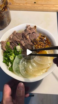 a person holding chopsticks over a bowl of food with meat and veggies