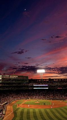 a baseball field at night with the sun setting in the distance and people playing on the field