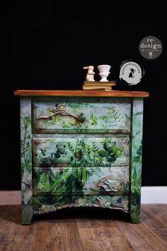 an old dresser painted with green plants and birds on it's side, next to a clock