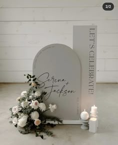 a bouquet of white flowers next to a memorial plaque and candles on the floor in front of a wooden wall