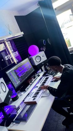 a man sitting in front of a keyboard on top of a white desk next to two monitors