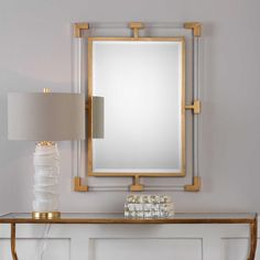 a table with a lamp and mirror on top of it next to a white wall