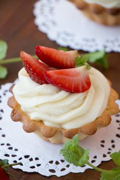 a cupcake with whipped cream and strawberries on top is sitting on a doily