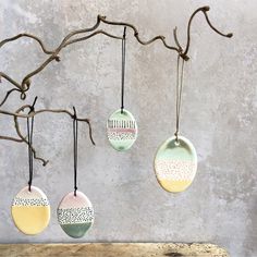 three ceramic ornaments hanging from a branch on a concrete wall, one is green and the other is yellow