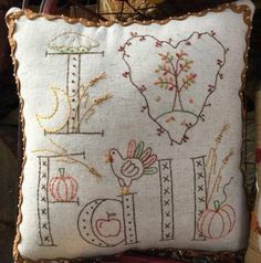 a white pillow with embroidered letters and pumpkins on the front, sitting on a chair