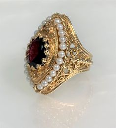 Garnet Ring, Garnet Jewelry, Garnet Engagement Ring, Garnet Ring for Women, Garnet Ring Vintage, Vintage Seed Pearl Ring, Garnet Gold Ring, Gemstone Ring Vintage An eye- catching regal vintage garnet ring featuring an oval shaped center stone weighing approximately 4.00 carats accented by 24 round seed pearls set in solid 14k yellow gold with intricate detailing.  *Ring size: US 7 3/4 *Ring weight: 15.15 Grams *Ring façade: 33X19mm *Center stone dimensions: 12X10mm