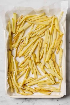 cooked french fries in a baking dish on a marble countertop with white parchment paper