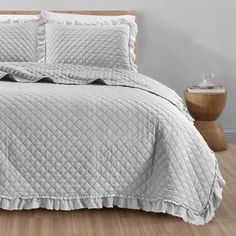 a bed with white bedspread and pillows on top of wooden floor next to wall