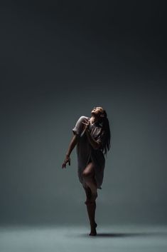 a woman is dancing in the dark with her hands behind her back and head down