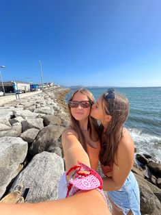 two young women taking a selfie on the rocks by the ocean with their camera