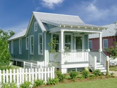 a white picket fence surrounding a small blue and pink house with a porch on the second floor