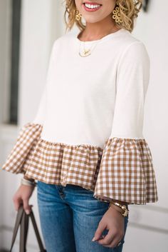 a woman wearing a white and brown checkered top with ruffles on the sleeves