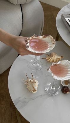 two wine glasses filled with seashells on top of a white marble coffee table