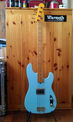 a blue electric guitar sitting on top of a wooden floor next to a shelf filled with cans