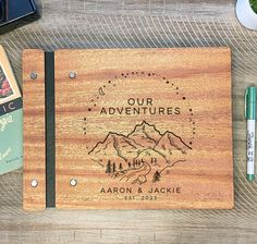 a personalized wooden notebook with the words our adventures engraved on it, surrounded by other items