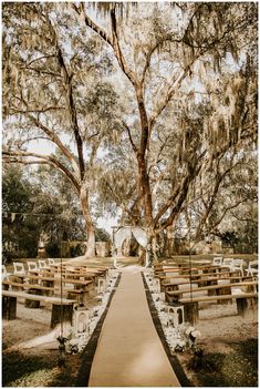 an outdoor ceremony setup with wooden benches and white tablecloths on the aisle, surrounded by trees