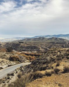 an empty road in the desert with mountains in the background and clouds in the sky