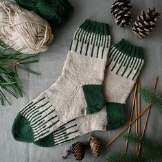 two green and white knitted socks next to pine cones, needles and yarn balls