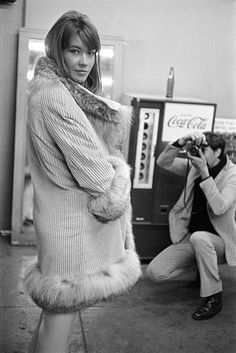 a woman in a fur coat taking a photo next to a man with a camera