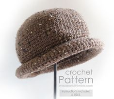 a crocheted brown hat on a metal stand with the word pattern above it