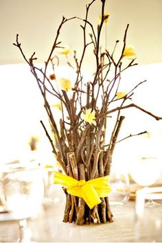 a vase filled with branches and flowers on top of a wooden table covered in yellow ribbon