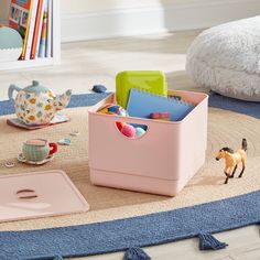 a toy horse is sitting on the floor next to a pink storage container with toys in it