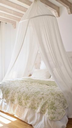 a white canopy bed sitting inside of a bedroom next to a wooden floor and window