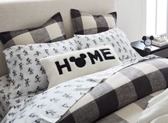 a bed with black and white checkered comforter, pillows and an alarm clock