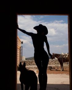 a woman standing next to a dog in front of a horse and carriage door with a cowboy hat on