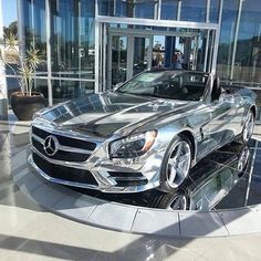 a silver mercedes sls parked in front of a glass building with people looking at it