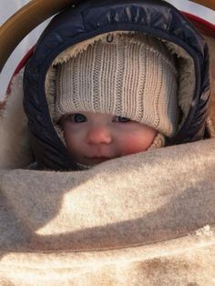 a baby in a stroller wearing a winter hat and coat, looking at the camera